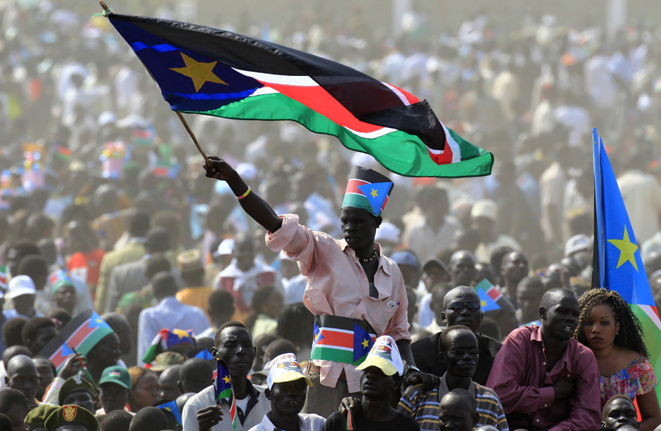 Person rises above a crowd, waving a Sudanese flag in the wind.