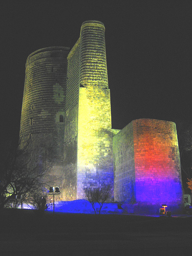 A stone building, illuminated with yellow, red, and blue lights at night. Maiden's Tower, Baku, Azerbaijan by Teuchterlad