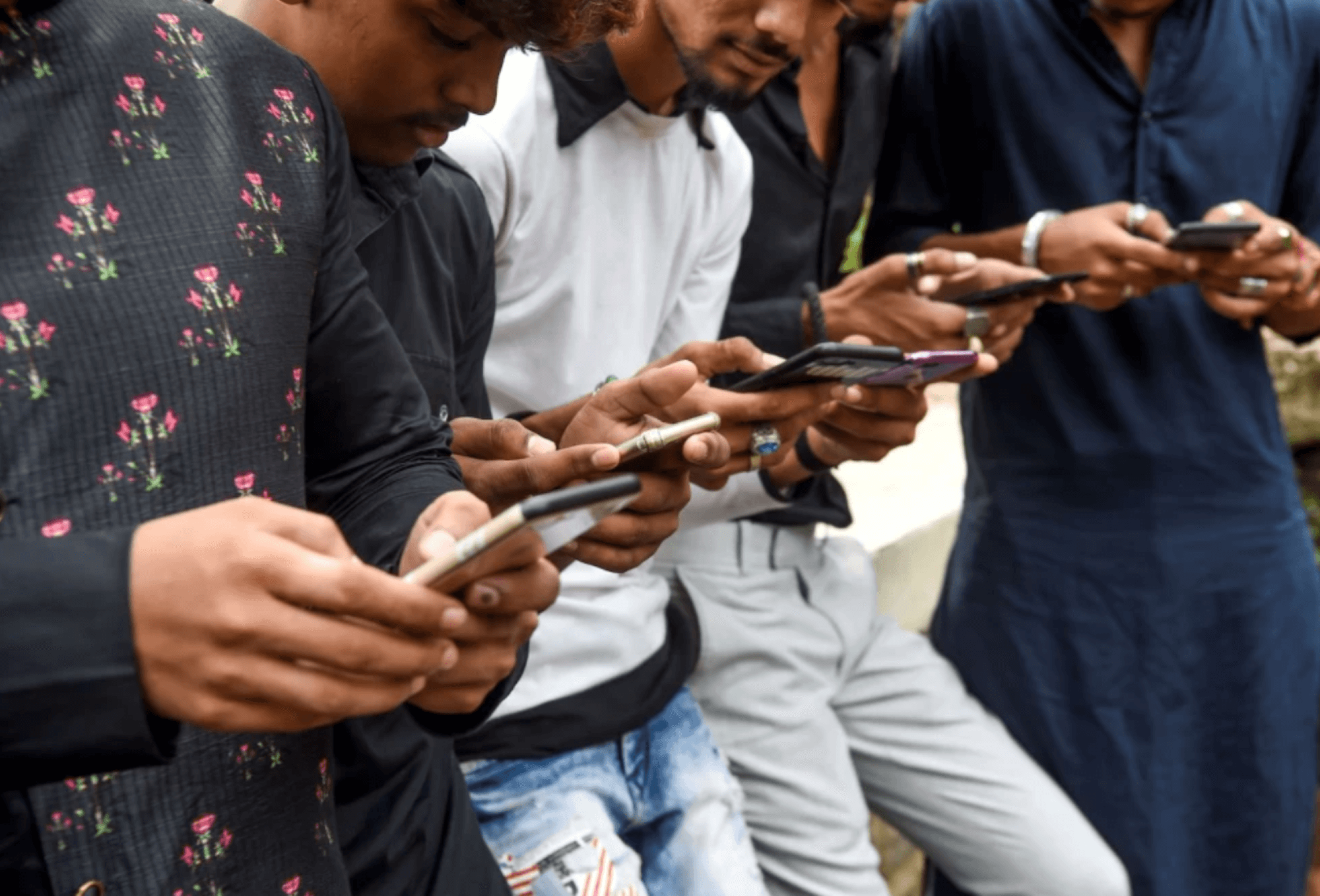 young Indian men stand in a line, looking at their phones. The camera is aimed at their hands. The picture was taken in Mumbai on November 10, 2019.