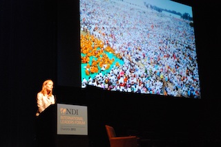 Speaker at the podium, in front of an abstract graphic.