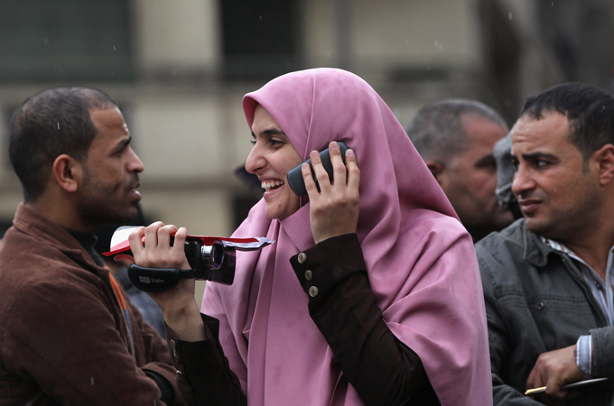 A women in a head scarf talks on the phone surrounded by men.
