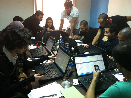 A group of 8-12 people, on laptops, sitting around a table.
