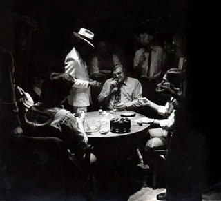 Black and white photo of people sitting around small card table.